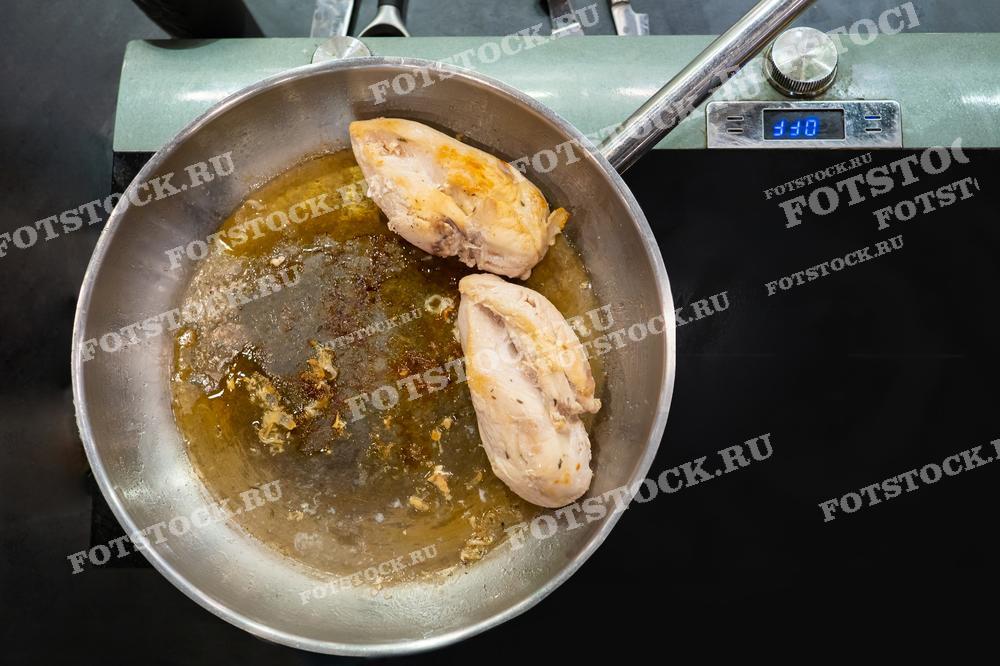 На изображении показаны две куриные грудки, обжаренные на сковороде в масле. Процесс приготовления пищи находится в активной стадии. Фотография иллюстрирует кулинарный процесс на профессиональной или домашней кухне.